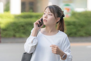 20 'li yaşlarda genç bir Japon kadın Aichi şehrinin Nagoya şehrinin sokaklarında akıllı bir telefonla konuşurken yürüyor.