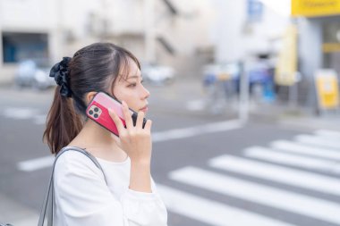 20 'li yaşlarda genç bir Japon kadın Aichi şehrinin Nagoya şehrinin sokaklarında akıllı bir telefonla konuşurken yürüyor.