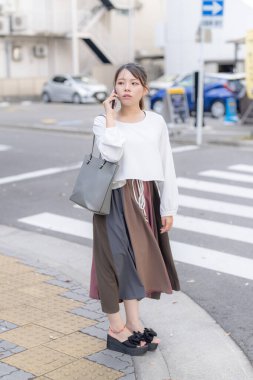 20 'li yaşlarda genç bir Japon kadın Aichi şehrinin Nagoya şehrinin sokaklarında akıllı bir telefonla konuşurken yürüyor.