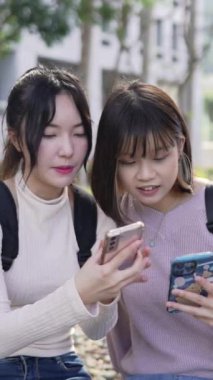 Tayvan, Taipei 'de bir üniversite kampüsünde oturan ve mutlu bir şekilde konuşan iki genç Tayvanlı kız öğrencinin yavaş çekimde dikey videosu.