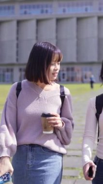 Tayvan, Taipei 'de bir üniversite kampüsünde konuşurken mutlu yürüyen iki genç Tayvanlı kız öğrencinin dikey ağır çekim videosu.
