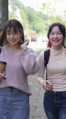 Tayvan, Taipei 'de bir üniversite kampüsünde konuşurken mutlu yürüyen iki genç Tayvanlı kız öğrencinin dikey ağır çekim videosu.