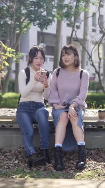 ベンチに座り 台湾の台北にある大学キャンパスで幸せに話す2人の台湾の女子大学生のスローモーション垂直ビデオ — ストック動画