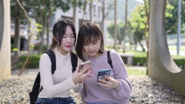 Tayvan 'ın Taipei şehrinde bir üniversite kampüsünde oturmuş sohbet eden ve selfie çeken iki Tayvanlı kız öğrencinin yavaş çekim videosu.