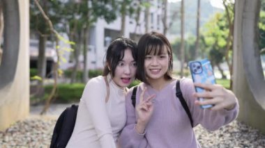 Tayvan 'ın Taipei şehrinde bir üniversite kampüsünde oturmuş sohbet eden ve selfie çeken iki Tayvanlı kız öğrencinin yavaş çekim videosu.