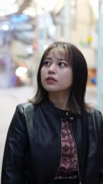 Okinawa 'nın Naha şehrinde turistik bir yer olan Kokusai-dori Caddesi' ndeki bir alışveriş sokağının arka sokağında 20 'li yaşlarında genç bir Japon kadının yürüdüğü dikey bir video.