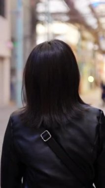 Okinawa 'nın Naha şehrinde turistik bir yer olan Kokusai-dori Caddesi' ndeki bir alışveriş sokağının arka sokağında 20 'li yaşlarında genç bir Japon kadının yürüdüğü dikey bir video.