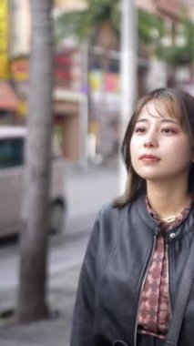 Okinawa 'nın Naha şehrinde turistik bir yer olan Kokusai Caddesi' nde 20 'li yaşlarda genç bir Japon kadının yürüdüğü dikey video.