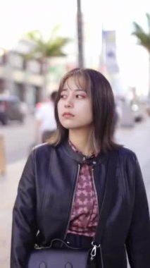 Okinawa 'nın Naha şehrinde turistik bir yer olan Kokusai Caddesi' nde 20 'li yaşlarda genç bir Japon kadının yürüdüğü dikey video.
