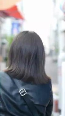 Okinawa 'nın Naha şehrindeki turistik bir eğlence merkezi olan Kokusai Caddesi' nde yirmili yaşlarında yürüyen genç bir Japon kadının dikey videosu.