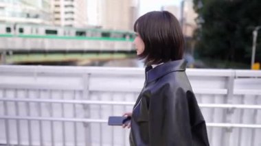 20 'li yaşlarında genç bir Japon kadın Gotanda, Shinagawa-ku, Tokyo' da tren istasyonunun yakınından geçen akıllı bir telefon kullanıyor.