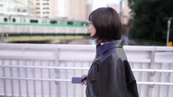 一名20多岁的日本年轻女子 她驾驶着一部智能手机 在东京神奈川谷田火车站附近有一列火车经过 — 图库视频影像