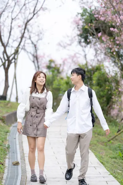 A young Taiwanese male and female couple in their 20s are taking a walk while talking happily in the mountains where the cherry blossoms of the Maokong are blooming, a tourist destination in Taiwan.