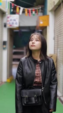 20 'li yaşlarının başında Okinawa bölgesinden genç bir Japon kadının Naha City, Okinawa' daki Kokusai-dori Caddesi civarındaki bir alışveriş caddesinde yürüdüğünü gösteren yavaş çekim dikey video.