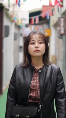 20 'li yaşlarının başında Okinawa bölgesinden genç bir Japon kadının Naha City, Okinawa' daki Kokusai-dori Caddesi civarındaki bir alışveriş caddesinde yürüdüğünü gösteren yavaş çekim dikey video.