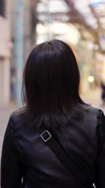 20 'li yaşlarının başında Okinawa bölgesinden genç bir Japon kadının Naha City, Okinawa' daki Kokusai-dori Caddesi civarındaki bir alışveriş caddesinde yürüdüğünü gösteren yavaş çekim dikey video.