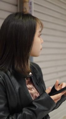 Okinawa 'nın Naha şehrindeki Kokusai-dori Caddesi yakınlarındaki bir alışveriş sokağında 20' li yaşlarda Okinawa bölgesinden genç bir Japon kadının akıllı telefonunu kullanırken ağır çekimde çekilmiş dikey videosu.