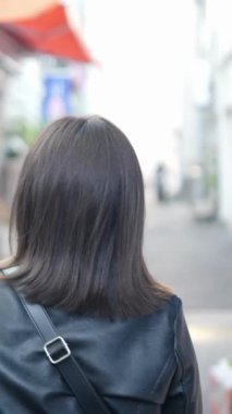 Okinawa 'nın Naha şehrinde Kokusai-dori Caddesi yakınlarında yürürken 20' li yaşlarda Okinawa bölgesinden genç bir Japon kadının akıllı telefon kullanmasının yavaş çekim dikey videosu.