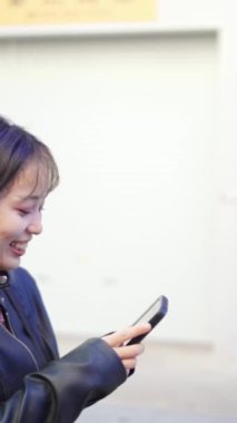 Okinawa 'nın Naha şehrinde Kokusai-dori Caddesi yakınlarında yürürken 20' li yaşlarda Okinawa bölgesinden genç bir Japon kadının akıllı telefon kullanmasının yavaş çekim dikey videosu.