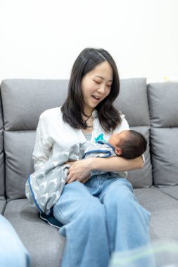 30 'larında gülümseyen Tayvanlı bir anne 8 günlük bir bebeği kanepeye oturtmuş.