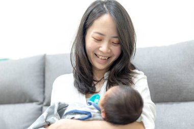 30 'larında gülümseyen Tayvanlı bir anne 8 günlük bir bebeği kanepeye oturtmuş.