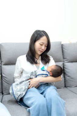 30 'larında gülümseyen Tayvanlı bir anne 8 günlük bir bebeği kanepeye oturtmuş.