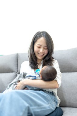 30 'larında gülümseyen Tayvanlı bir anne 8 günlük bir bebeği kanepeye oturtmuş.