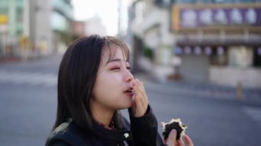 Okinawa Bölgesi 'nden genç bir Japon kadın 20' li yaşlarında Okinawa sokak yemeği domuz yumurtalı pirinç topları yiyor Naha City, Okinawa 20 'de Kokusai Caddesi' nde.