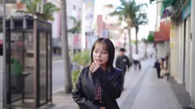 Okinawa bölgesinden 20 'li yaşlarda, kışlık kıyafetleriyle genç bir Japon kadın Naha City, Okinawa' da Kokusai Caddesi 'nde gülümseyerek yürüyor.