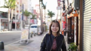 Okinawa bölgesinden 20 'li yaşlarda, kışlık kıyafetleriyle genç bir Japon kadın Naha City, Okinawa' da Kokusai Caddesi 'nde gülümseyerek yürüyor.