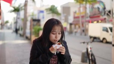 Okinawa bölgesinden genç bir Japon kadın 20 'li yaşlarda, kışlık kıyafetleriyle sokak yemekleri yiyor. Naha City, Okinawa' da Kokusai Caddesi 'nde bir sürü sataandagi var.