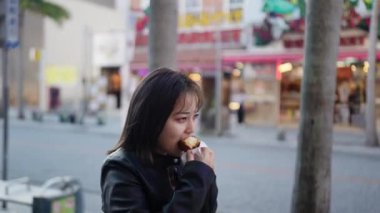 Okinawa bölgesinden genç bir Japon kadın 20 'li yaşlarda, kışlık kıyafetleriyle sokak yemekleri yiyor. Naha City, Okinawa' da Kokusai Caddesi 'nde bir sürü sataandagi var.