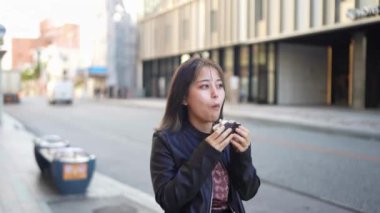 Okinawa 'nın Naha şehrinde Kokusai Caddesi' nde yürürken, 20 'li yaşlarda, kışın giyinmiş, sokak yemeği yiyen domuz yumurtalı pirinç topları yiyen bir kadının yavaş çekim videosu.