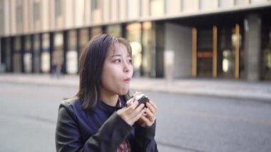 Okinawa 'nın Naha şehrinde Kokusai Caddesi' nde yürürken, 20 'li yaşlarda, kışın giyinmiş, sokak yemeği yiyen domuz yumurtalı pirinç topları yiyen bir kadının yavaş çekim videosu.