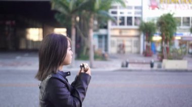 Okinawa 'nın Naha şehrinde Kokusai Caddesi' nde yürürken, 20 'li yaşlarda, kışın giyinmiş, sokak yemeği yiyen domuz yumurtalı pirinç topları yiyen bir kadının yavaş çekim videosu.
