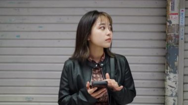 Okinawa 'nın Naha şehrinde Kokusai Caddesi' nde bir akıllı telefonu işleten 20 'li yaşlarda, kışlık kıyafetleriyle bir Okinawalı kadının yavaş çekim videosu. 