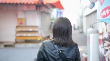 Okinawa, Naha City 'de bir alışveriş caddesi nead Kokusai Caddesi' nde yürürken 20 'li yaşlarda, akıllı telefon kullanan bir kadının yavaş çekim videosu.