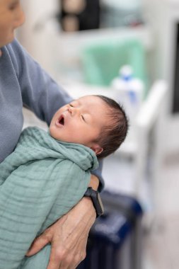 Büyükanne yeşil bir naylona sarılı Tayvanlı bir bebek tutuyor.