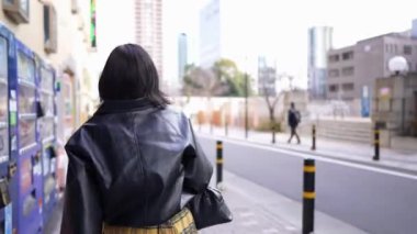 20 'li yaşlarda Japon bir kadın kışın akıllı telefonunu kullanırken Gotanda İstasyonu, Shinagawa-ku, Tokyo civarında nehir kenarında yürüyor.