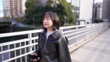 20 'li yaşlarda Japon bir kadın kışın akıllı telefonunu kullanırken Gotanda İstasyonu, Shinagawa-ku, Tokyo civarında nehir kenarında yürüyor.