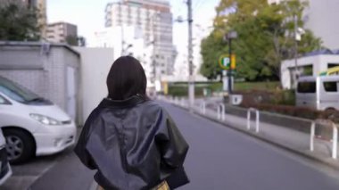 20 'li yaşlarda Japon bir kadın kışın akıllı telefonunu kullanırken Gotanda İstasyonu, Shinagawa-ku, Tokyo civarında nehir kenarında yürüyor.