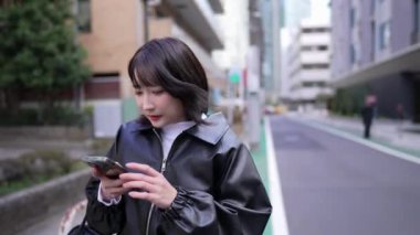 20 'li yaşlarda Japon bir kadın Gotanda İstasyonu, Shinagawa-ku, Tokyo' da kışın akıllı telefonunu durdurup işletiyor.