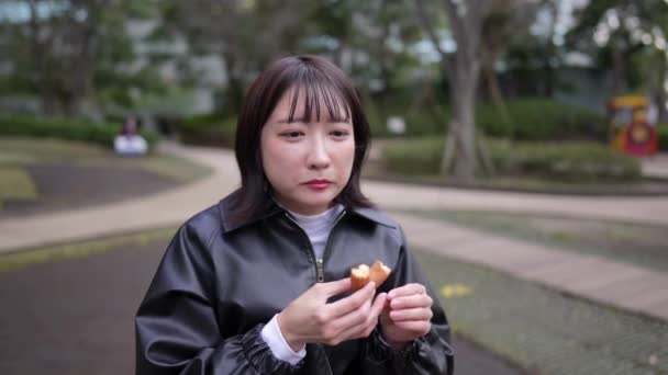 一名20多岁的日本妇女 冬天坐在东京新川谷田站附近的公园里吃甜甜圈 — 图库视频影像