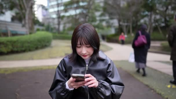 一位20多岁的日本妇女坐在Gotanda车站附近的一个公园里 — 图库视频影像