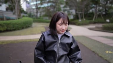 Japon bir kadının kışın Gotanda İstasyonu, Shinagawa-ku, Tokyo yakınlarındaki bir parkta oturup akıllı telefonunu kullanmasını gösteren yavaş çekim videosu.