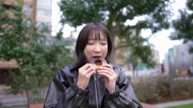 20 'li yaşlarında Japon bir kadının kışın Shinagawa-ku, Tokyo' daki Gotanda İstasyonu 'nun etrafındaki bir parkta donut yediği yavaş çekim videosu.