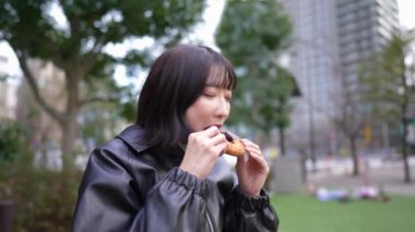 20 'li yaşlarında Japon bir kadının kışın Shinagawa-ku, Tokyo' daki Gotanda İstasyonu 'nun etrafındaki bir parkta donut yediği yavaş çekim videosu.