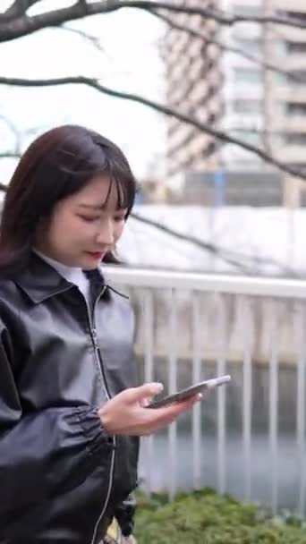 20代の若い日本人女性が 冬にスマートフォンで東京品川区五田駅を歩き回る垂直ビデオ — ストック動画