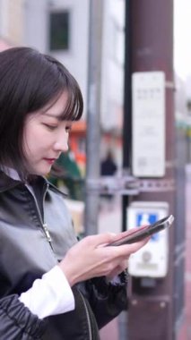 20 'li yaşlarda genç bir Japon kadının Gotanda İstasyonu, Shinagawa-ku, Tokyo' da kışın durup akıllı telefonunu kullanmasının dikey videosu.