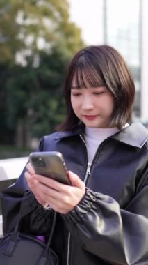 20 'li yaşlarda genç bir Japon kadının Gotanda İstasyonu, Shinagawa-ku, Tokyo' da kışın durup akıllı telefonunu kullanmasının dikey videosu.